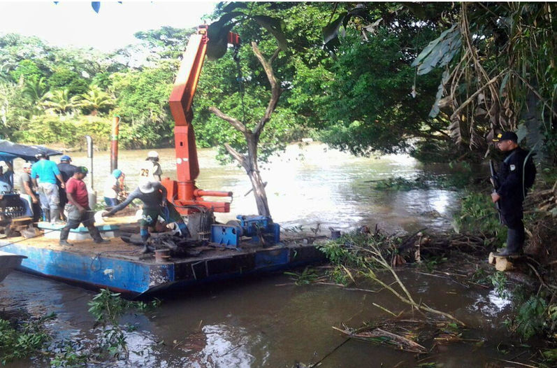 Nicaraguan workers pull a tree from the Rio San Juan near the Costa Rican side of the river as a Costa Rican police officer looks on. (Foreign Ministry Photo)